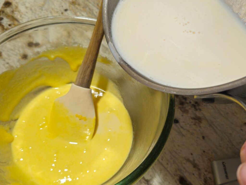 pouring hot milk over egg yolk and sugar