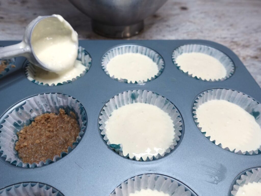 cookie scoop placing cheesecake filling into each cupcake liner