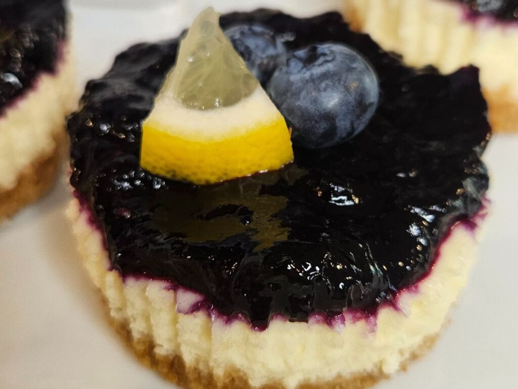 A close up picture of a mini lemon cheesecake with a lavender blueberry compote