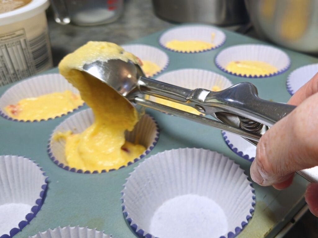 using a cookie scoop to place cupcake batter into liners