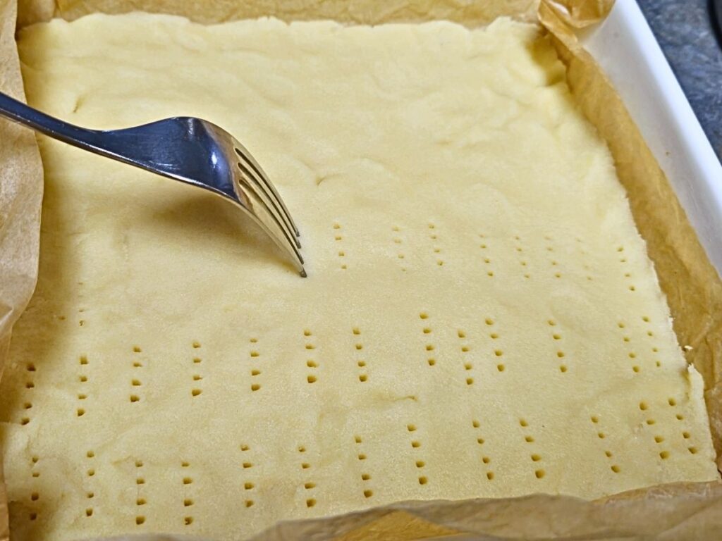 a fork pocking holes into the raw shortbread base